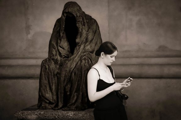 Frau in schwarzem Kleid steht neben einer dunklen, schattenhaften Statue.