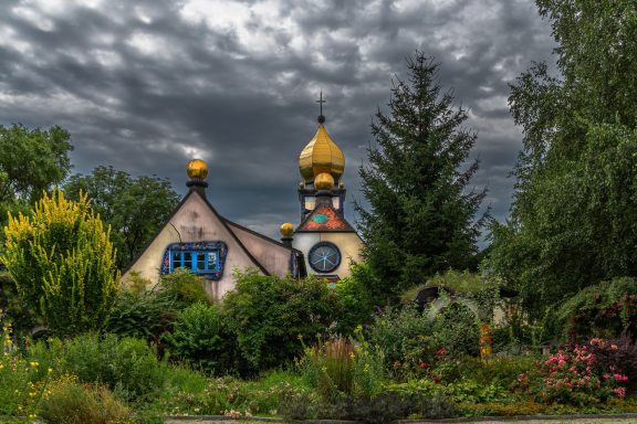 Fantasievolle Architektur mit goldenen Kuppeln und bunten Fenstern in einem Garten.